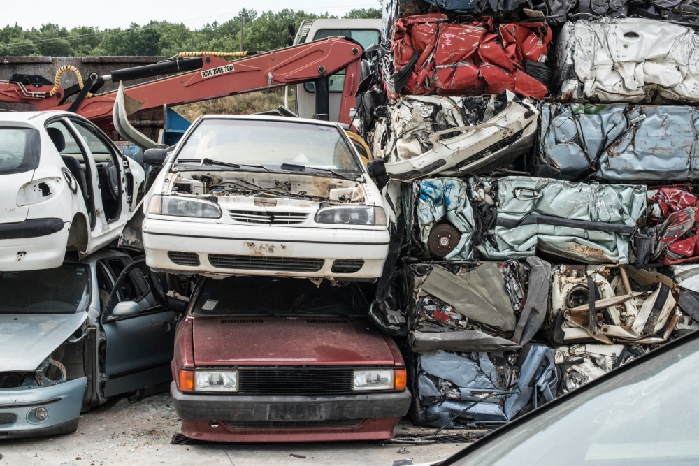 A stack of crushed and mangled cars sits next to a line of old vehicles awaiting processing at an eco-friendly vehicle recycling facility.