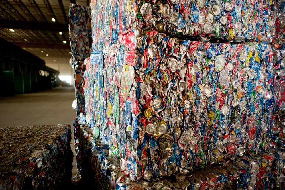 Large, rectangular bales of crushed aluminum soda cans stacked inside a recycling warehouse.