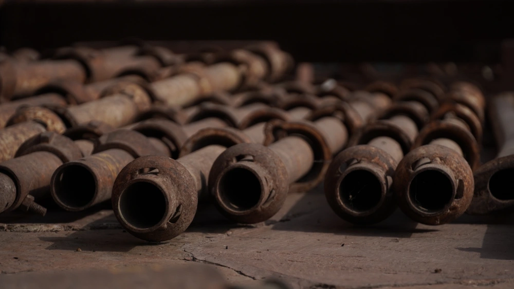 Rows of old, rusted metal pipes and industrial joints laid out on a concrete surface at a recycling facility.